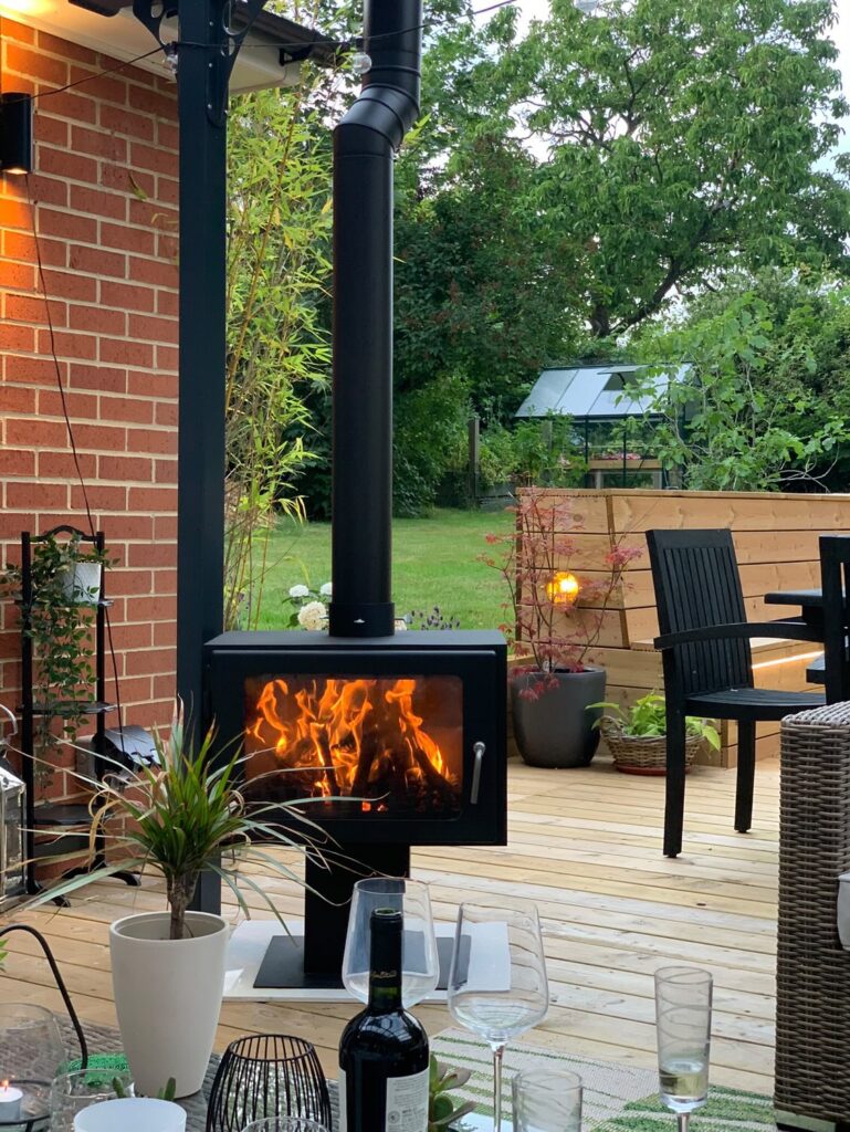 Outdoor log burner with chimney installed in pergola covered patio area